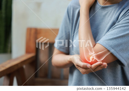 Close-up woman holding painful injured elbow with red inflamed spot and X-ray bone skeleton overlay. Medical concept of joint pain, fracture, arthritis, tendonitis, muscle injury, outdoor background. Close-up woman holding painful injured elbow with red inflamed spot and X-ray bone skeleton overlay. Medical concept of joint pain, fracture, arthritis, tendonitis, muscle injury, outdoor background. 135944142