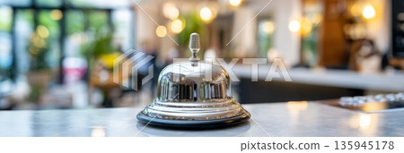 Polished receptionist bell on glossy counter in upscale hotel lobby, warm tones and cinematic bokeh creating inviting atmosphere 135945178
