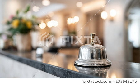 Polished metal service bell on glossy reception counter in upscale hotel lobby, showcasing elegant ambiance and warm lighting for hospitality concept 135945179
