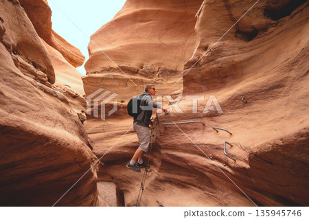 The young man is climbing a canyon in a dry riverbed in the desert. Red Canyon in the Negev desert, Israel The young man is climbing a canyon in a dry riverbed in the desert. Red Canyon in the Negev desert, Israel 135945746