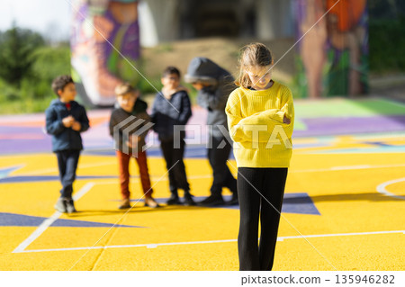Girl feeling excluded by peer group on colorful playground Girl feeling excluded by peer group on colorful playground 135946282