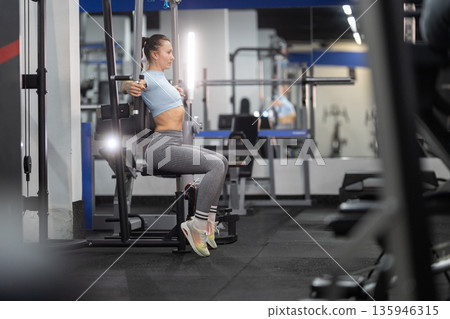 Woman exercising chest muscles on fly machine 135946315