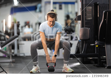 Woman exercising with kettlebell in modern gym Woman exercising with kettlebell in modern gym 135946349