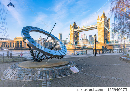 A large sundial stands prominently by the River Thames near Tower Bridge. The sun casts a shadow, showcasing the unique design against the backdrop of iconic London architecture. A large sundial stands prominently by the River Thames near Tower Bridge. The sun casts a shadow, showcasing the unique design against the backdrop of iconic London architecture. 135946675
