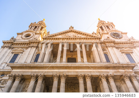 St. Pauls Cathedral stands tall in London. Visitors gather around the front portal. The sun shines on the historic building, highlighting its impressive architecture. 135946683