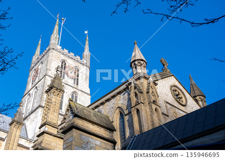 Southwark Cathedral is seen during a sunny day in London. The tower and stone details of the building are visible against the clear blue sky, showcasing its historic architecture. 135946695