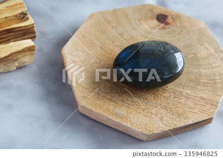 Polished labradorite stone with iridescent blue and green reflections, placed on a natural wooden base with a neutral background. Polished labradorite stone with iridescent blue and green reflections, placed on a natural wooden base with a neutral background. 135946825