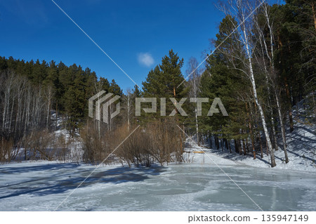 Frozen lake with forest on the shore. Winter landscape with snow forest lake and blue sky perfect for nature travel and climate articles. Frozen lake with forest on the shore. Winter landscape with snow forest lake and blue sky perfect for nature travel and climate articles. 135947149
