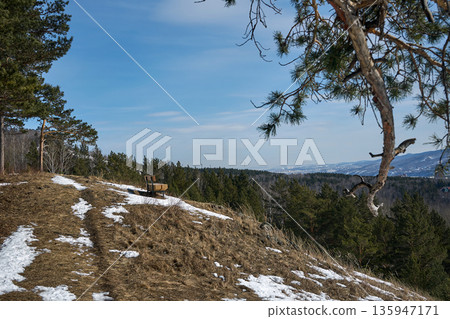 Wooden bench on a snowy hillside overlooking a forest. Scenic landscape view from a mountain in late winter or early spring. Wooden bench on a snowy hillside overlooking a forest. Scenic landscape view from a mountain in late winter or early spring. 135947171