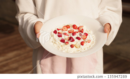 White plate with cottage cheese, strawberries, and raspberries in hands girl, ready to eat on a sunny day. 135947289