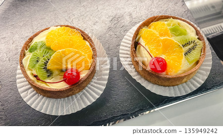 Two gourmet fruit tarts with custard filling, topped with fresh kiwi slices, orange, and a cherry. 135949242