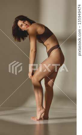 Natural female body in brown lingerie posing in studio background Natural female body in brown lingerie posing in studio background 135949474