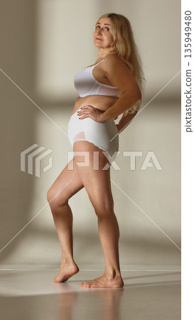 Confident mature woman in white underwear standing in studio. Confident mature woman in white underwear standing in studio. 135949480