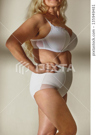 Mature woman posing confidently in white lingerie in studio. Mature woman posing confidently in white lingerie in studio. 135949481