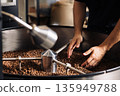The hands of a male employee wanted to scoop fresh beans from the machine drum. Process of checking the quality of roasted beans. 135949788