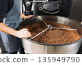An unrecognizable male worker standing at the roasting coffee machine and looking at the drum full of coffee beans  135949790