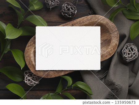 Horizontal card mockup on brown wooden tray near green leaves and grey fabric  top view 135950673