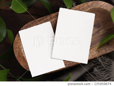 Vertical cards on brown wooden tray near green leaves and grey fabric top view, boho mockup 135950674