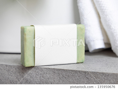 Green soap bar with blank label near white bath towels and basin on grey stone, mockup 135950676