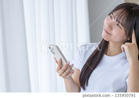 Young woman holding a smartphone and thinking 135950791