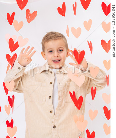 Smiling child waving hands surrounded by red hearts on white background. Friendly gesture, love, joy and Valentines Day concept Smiling child waving hands surrounded by red hearts on white background. Friendly gesture, love, joy and Valentines Day concept 135950841