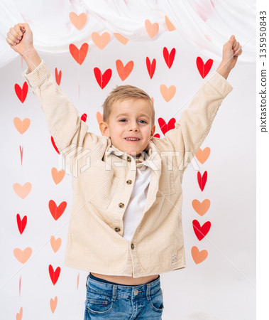Happy smiling child with raised hands surrounded by red hearts on white background. Joy, love, positive emotions and childhood happiness concept Happy smiling child with raised hands surrounded by red hearts on white background. Joy, love, positive emotions and childhood happiness concept 135950843