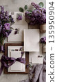 Elegant flat lay of wedding invitation cards. Set includes craft envelopes, paper invitations, purple ribbons, a name place card, and floral decoration. purple lilac flowers. Vertical top view 135950904