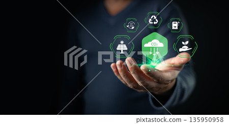 A person holds glowing eco-friendly icons representing CO2 reduction, renewable energy, recycling, green fuel, and sustainability, symbolizing net zero goals and environmental responsibility. 135950958