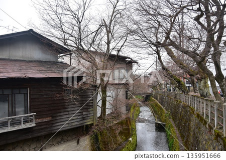 日本岐阜縣高山市的古老街景。古老的房屋散發著歷史氣息。高山春季祭典期間的清晨景象。一條小溪穿過城市。 日本岐阜縣高山市的古老街景。古老的房屋散發著歷史氣息。高山春季祭典期間的清晨景象。一條小溪穿過城市。 135951666