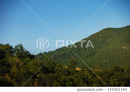 A sweeping mountain landscape in August 2025, with tiered, wooded hills under a clear summer sky. A sweeping mountain landscape in August 2025, with tiered, wooded hills under a clear summer sky. 135952169