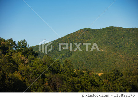 A sweeping mountain landscape in August 2025, with tiered, wooded hills under a clear summer sky. 135952170