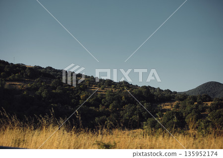 A sweeping mountain landscape in August 2025, with tiered, wooded hills under a clear summer sky. A sweeping mountain landscape in August 2025, with tiered, wooded hills under a clear summer sky. 135952174