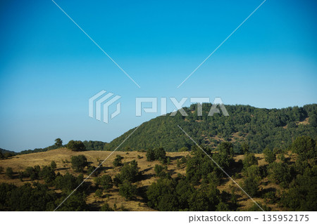 A sweeping mountain landscape in August 2025, with tiered, wooded hills under a clear summer sky. A sweeping mountain landscape in August 2025, with tiered, wooded hills under a clear summer sky. 135952175