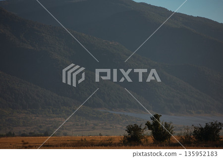 A sweeping mountain landscape in August 2025, with tiered, wooded hills under a clear summer sky. A sweeping mountain landscape in August 2025, with tiered, wooded hills under a clear summer sky. 135952183
