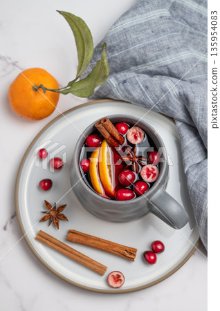 A cup of red mulled wine with cinnamon, orange and cranberry on a plate on a marble background A cup of red mulled wine with cinnamon, orange and cranberry on a plate on a marble background 135954083