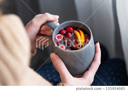 A woman holds a mug of non-alcoholic mulled wine or a spicy hot drink with orange A woman holds a mug of non-alcoholic mulled wine or a spicy hot drink with orange 135954085