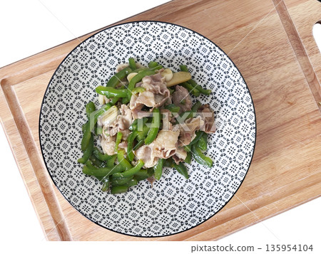 Still of a plate of stir-fried green bell pepper and thinly sliced pork, served in a patterned bowl on a wooden cutting board 135954104