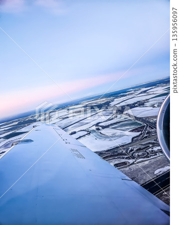 Airplane wing over a snow-covered landscape and highway at sunrise. Aerial view. 135956097