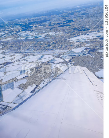 Aerial view from an airplane wing of a snow-covered city and winter landscape. 135956104