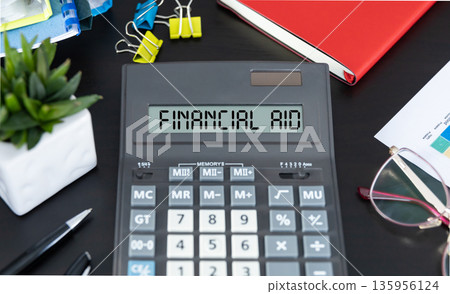 The text FINANCIAL AID written on calculator display on office table. 135956124