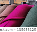 Close-up view of a row of colored womens wool coats hanging neatly on a rack in a store. 135956125