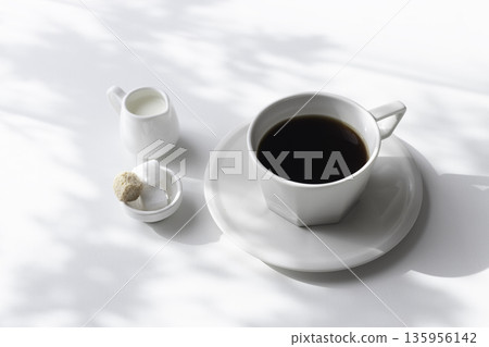 Coffee, milk, and sugar cubes on a white background. Shadows from sunlight filtering through the trees and white space. Coffee, milk, and sugar cubes on a white background. Shadows from sunlight filtering through the trees and white space. 135956142