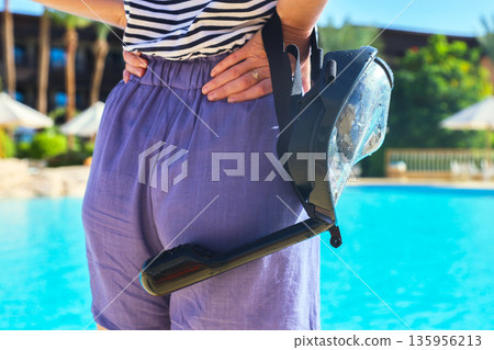 Close-Up of a Woman Holding a Snorkeling Mask Against the Background of a Sparkling Pool, Ready for an Exciting Underwater Adventure 135956213