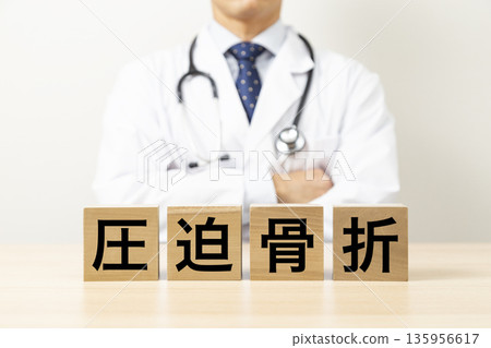 一塊寫著「壓迫性骨折」的磚塊和一位醫生 一塊寫著「壓迫性骨折」的磚塊和一位醫生 135956617