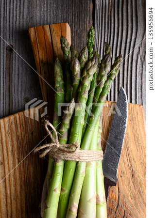 Bundled green asparagus tied with knife on wooden cutting board Bundled green asparagus tied with knife on wooden cutting board 135956694