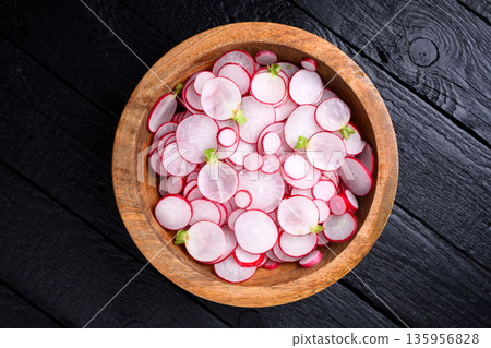 Overhead view of radish slices in wooden bowl on black surface Overhead view of radish slices in wooden bowl on black surface 135956828