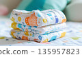 Soft patterned newborn diapers neatly stacked on cozy nursery bedding. Colorful patterns. Baby nesting, comfort, essential hygiene, organization, welcoming new baby home, early parenthood preparation. 135957823