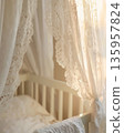 Beautiful nursery crib draped with delicate soft lace canopy in warm natural light. Heartfelt baby nesting preparation, cozy comfort textures. Serene newborn sleeping space environment. Peaceful care. 135957824