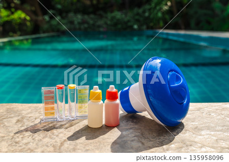 Pool water testing kit, chemical bottles, and floating dispenser on pool edge for swimming pool maintenance and water quality control 135958096
