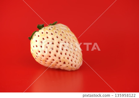 Unique white pineberry strawberry with red seeds on a vibrant red background 135958122